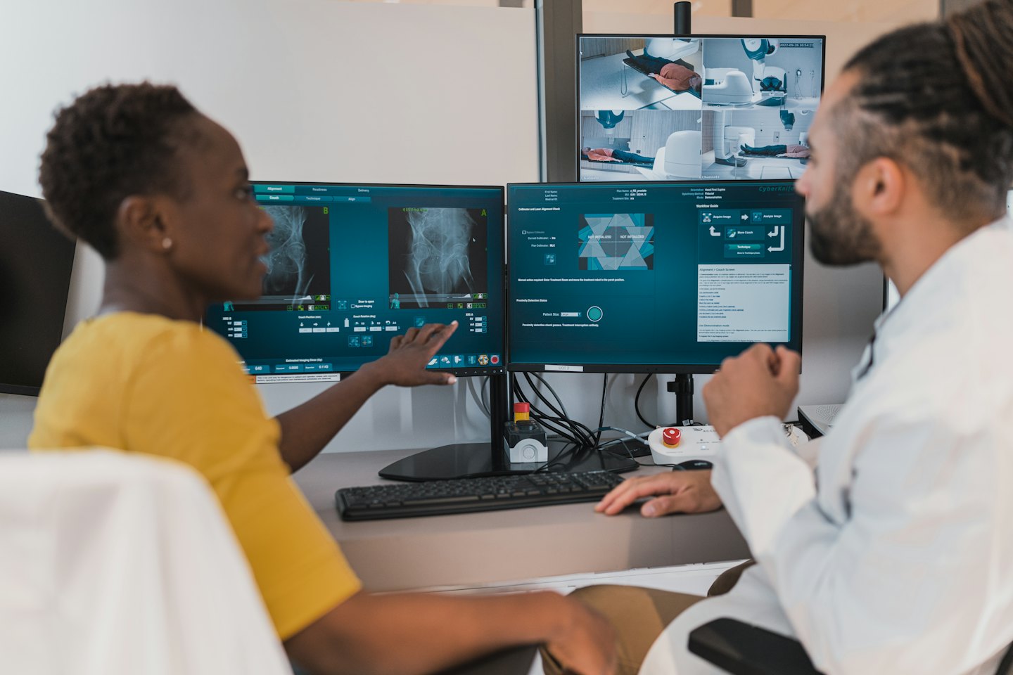 Two medical professionals review patient scans on multiple computer monitors.
